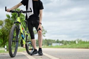 an injured male cyclist walking along the street with his bike. knee pain, fell off the bike, accident during cycling